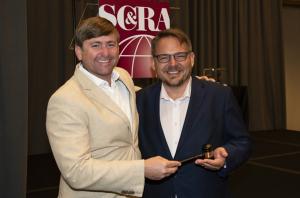 Picture of Matthew Rix receiving a gavel from C&RA Crane & Rigging Group Chairman Jeremy Landry in celebration of his new committee appointment.  Both men are smiling.
