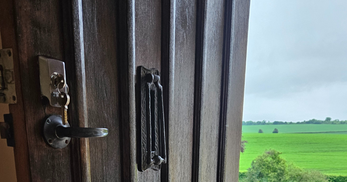 Open wooden door with lock, can see green fields