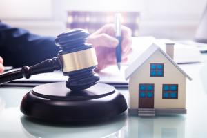 Gavel With Sound Block And House Model Over Desk In Front Of A Businessperson